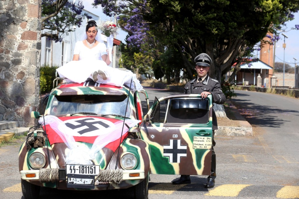 The Mexican couple riding an old Volkswagen Beetle with a swastika to their Nazi-themed wedding.