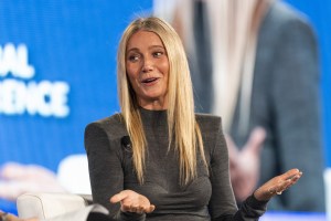 Gwyneth Palrow wearing a gray turtleneck gestures with her hands up.