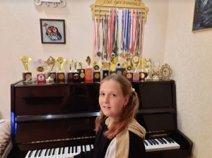 10-year-old Darinka Monko sitting in front of her piano with the medals and trophies she has won for piano, theater, chess, and singing. Credit: Tatiana Monko