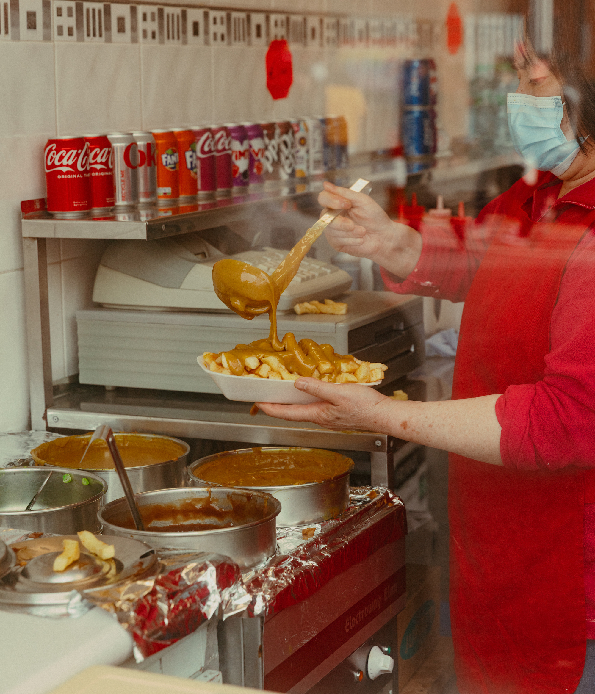 A woman ladles curry sauce onto chips at Sing Fong, Liverpool