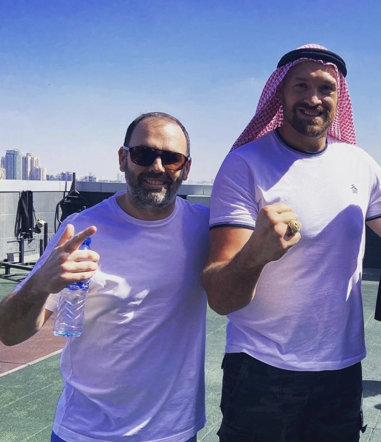 Zwei Männer, Daniel Kinahan und Tyson Fury, posieren in weißen T-Shirts in der Sonne vor einer Skyline für die Kamera