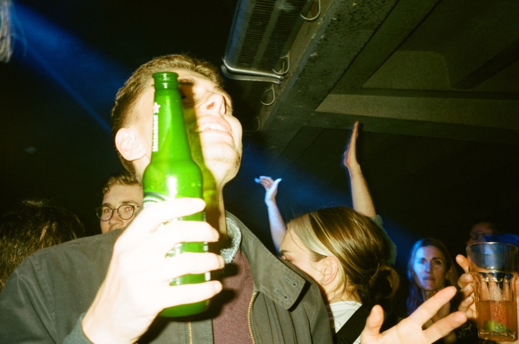 A man experiencing the hangover effect while holding a bottle of beer