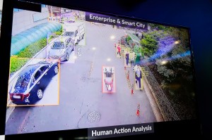 A monitor showing cars and pedestrians on a city street identified by bounding boxes.