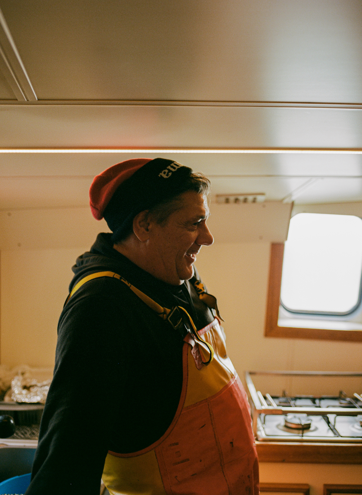 Ostend, fishing, photography - Photograph of a fisherman in a black and red beanie hat, wearing yellow rubber dungarees stood inside a fishing vessel.