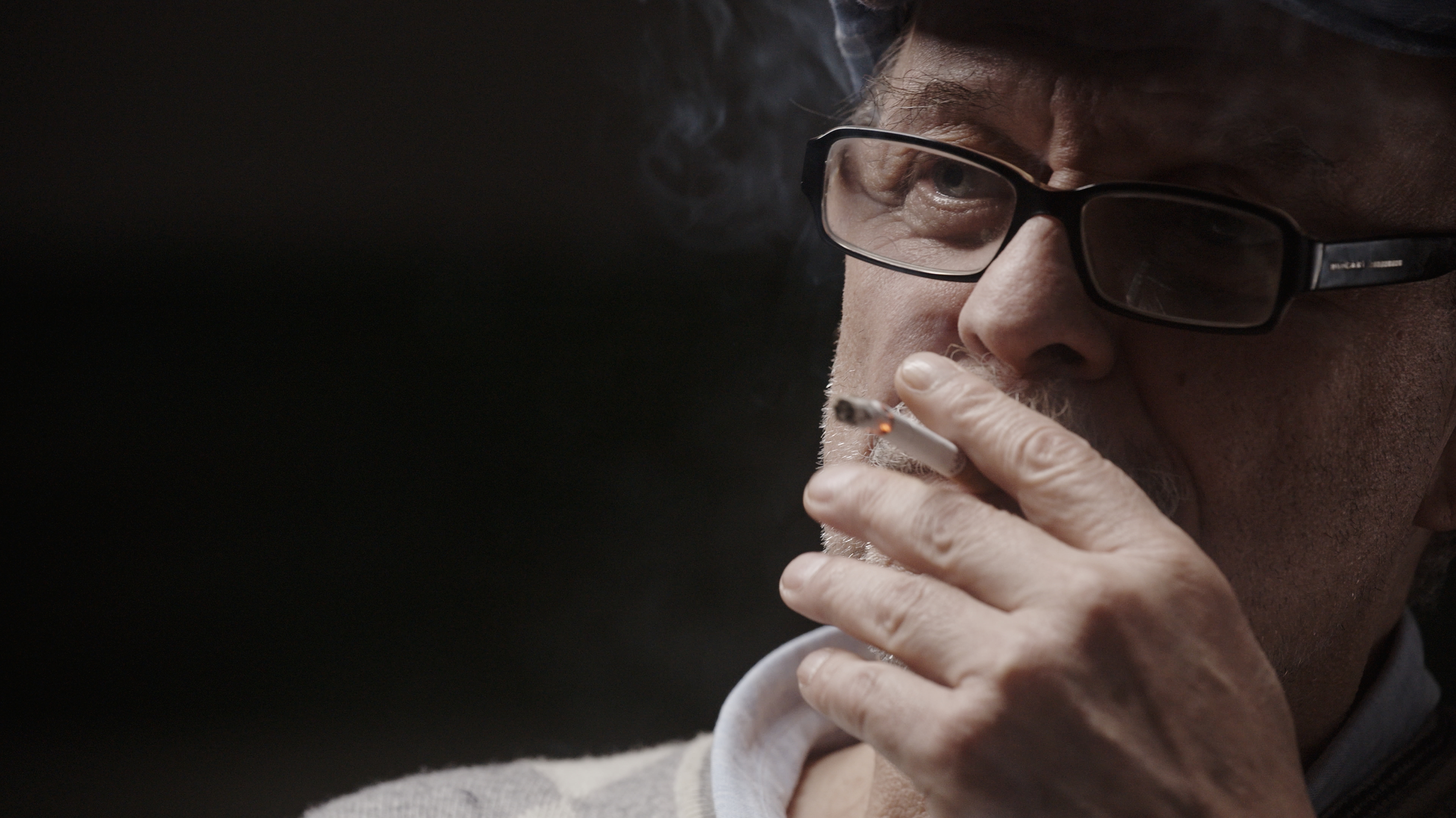 Renato Vallanzasca – close-up of an old man smoking a cigarette in a dark room.