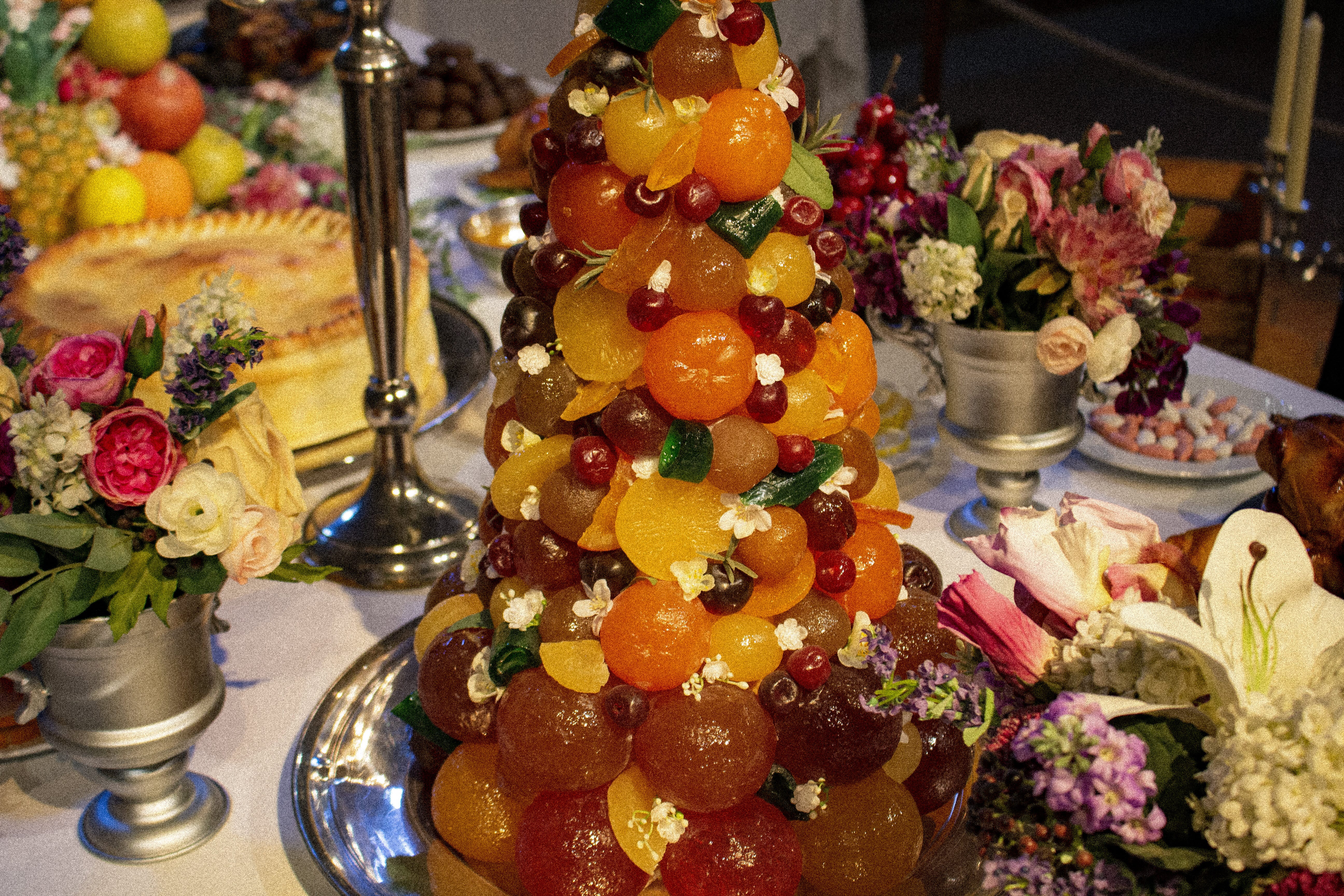 Château de Vaux-le-Vicomte – Tower of candied fruit, laid on a table with a white cloth, surrounded by flower vases with a meat pie in the background.