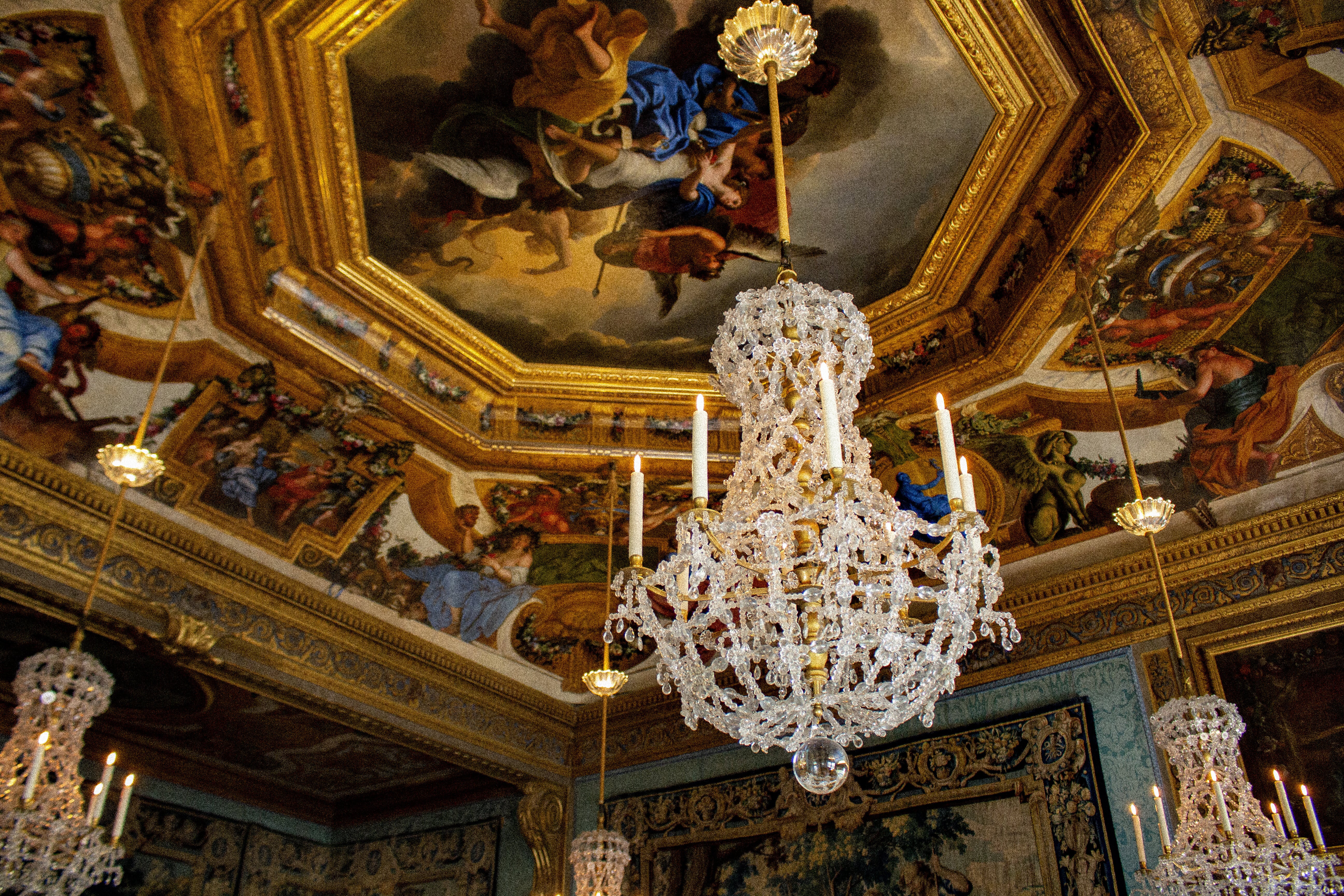 Château de Vaux-le-Vicomte – Photo of the ceilings with baroque paintings, different mouldings, lots of gold details and chandeliers hanging from it.