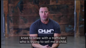 Screenshot shows tim Ballard sitting in a chair in an OUR t-shirt, the caption underneath reads 'knee to knee with a trafficker who is trying to sell me a child"