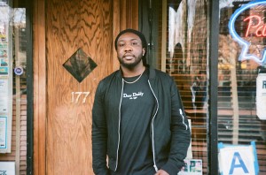 Randy Robinson, known to Ray's regulars as Door Daddy Randy, stares directly at the camera with hands in pocket. He's wearing a black jacket and black t-shirt.