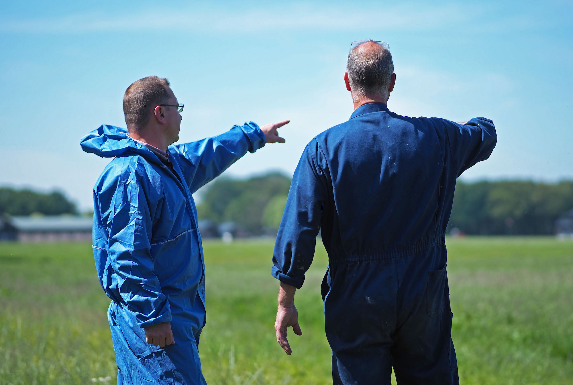 Leon in gesprek met de pluimveehouder, ze dragen blauwe overalls.