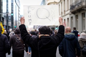 A man holds a placard with 'Trump loves QAnon' written while he protests against the compulsory vaccination campaign on January 9, 2022 in Brussels, Belgium. (Thierry Monasse/Getty Images)