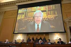 Photo shows the House Chambers with a big screen showing an image of John Eastman, a yelling white man with white hair.