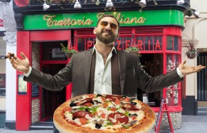 mafia food: cigar-smoking man in a suit, standing in front of a pizzeria with open hands with a pizza in the foreground.