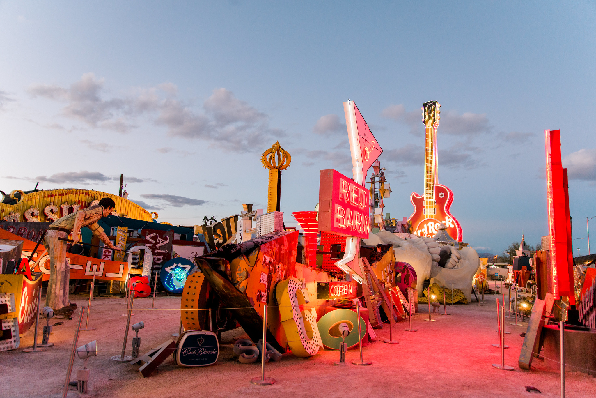 A photo of an arrangement of glowing antique neon signs at the Neon Museum against a dimming sky