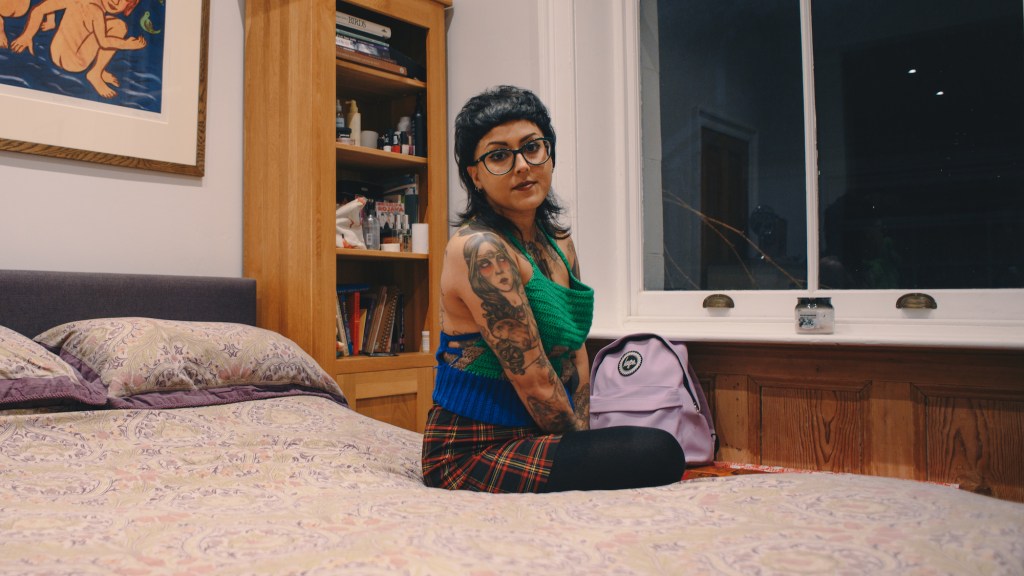 A nonbinary South Asian person sitting on bed