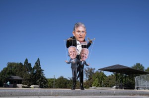 A protester depicts Manchin playing Schumer and Biden like puppets.