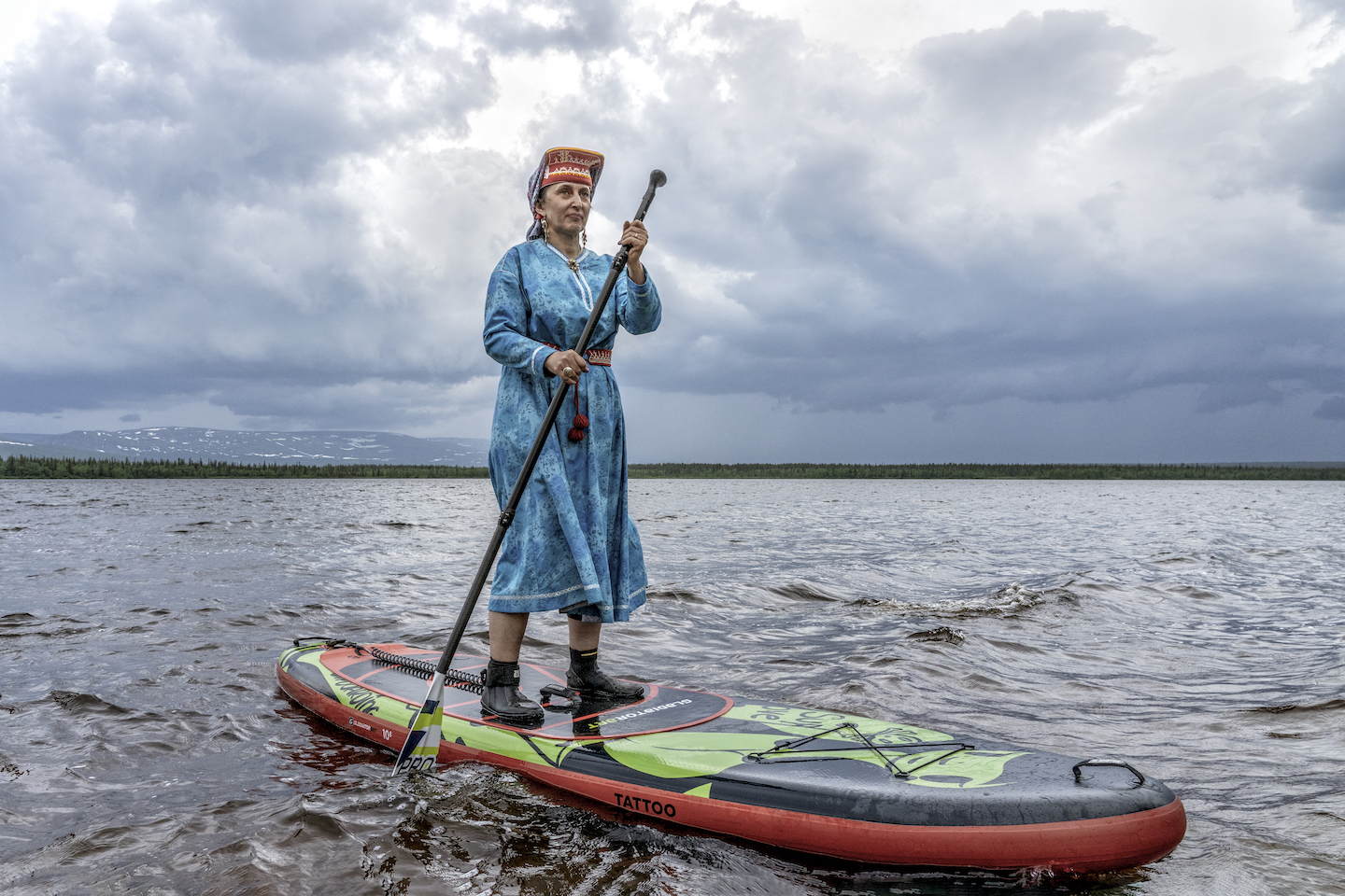 A Saami woman paddleboards over water.