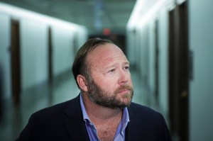 Alex Jones is seen in an endless hallway, looking to his left and appearing thoughtful.