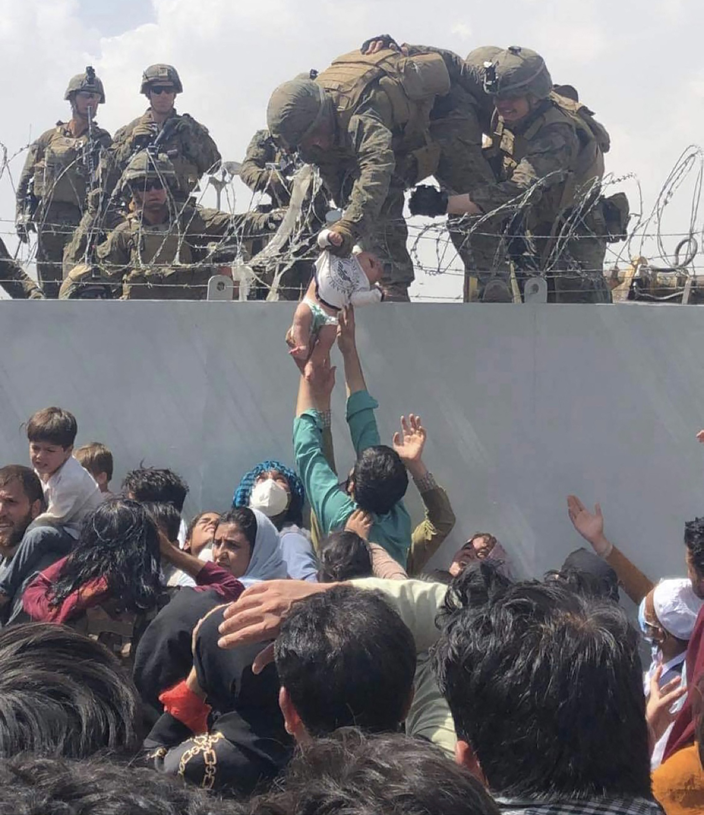 This image made available to AFP on August 20, 2021 by Human Rights Activist Omar Haidari, shows a US Marine grabbing an infant over a fence of barbed wire during an evacuation at Hamid Karzai International Airport in Kabul on August 19, 2021. A Pentagon official confirmed Friday that US evacuation operations from Kabul's airport have been stalling because the receiving base in Qatar is overflowing and could not receive evacuees. Photo: Courtesy of Omar Haidiri/AFP via Getty Images