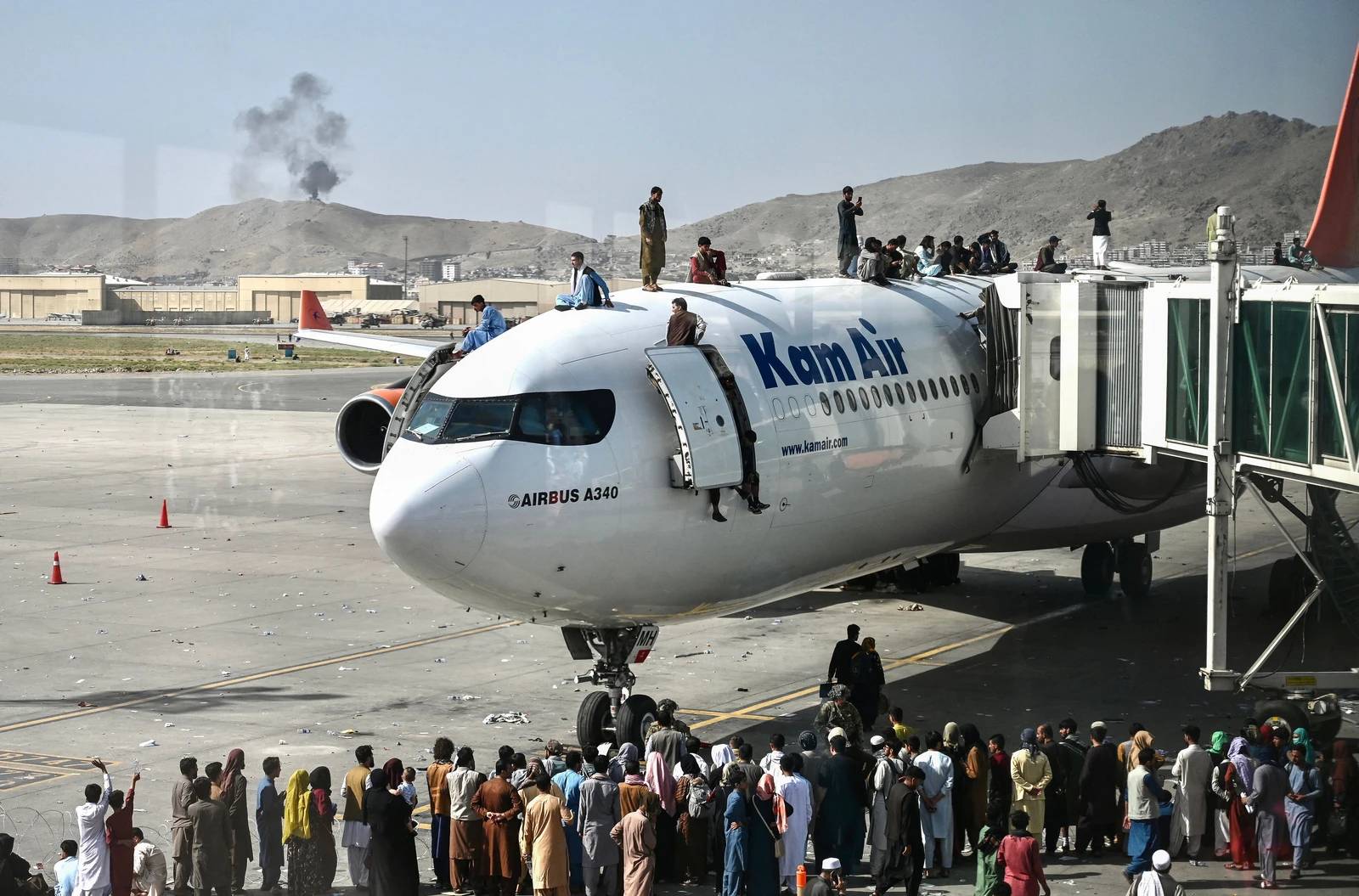 Afghan people climb atop a plane as they wait at the Kabul Airport on August 16, 2021. After a stunningly swift end to Afghanistan’s 20-year war, thousands of people mobbed the city’s airport trying to flee the group’s feared hardline brand of Islamist rule. Photo: Wakhil Kohsar/AFP via Getty Images