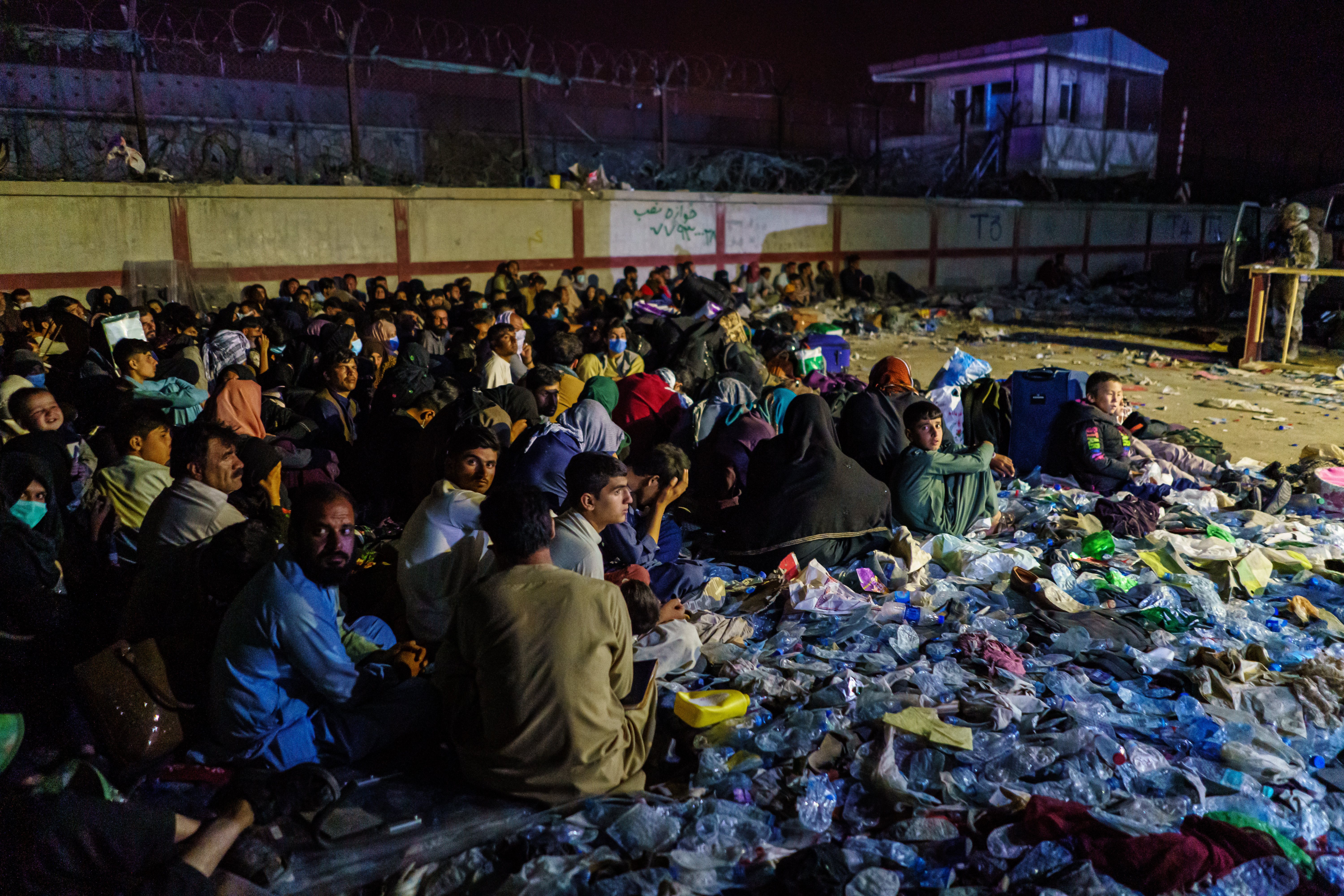 Afghan refugees crouch in a group as British military secure the perimeter outside the Baron Hotel, near the Abbey Gate, in Kabul, Afghanistan on August 26, 2021. Photo: Marcus Yam/Los Angeles Times