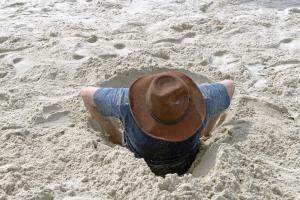 A man descends into a hole he has dug on the beach.