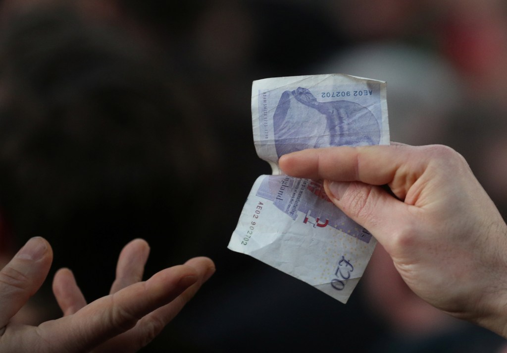 A hand passing a 20 pound note to another hand hand