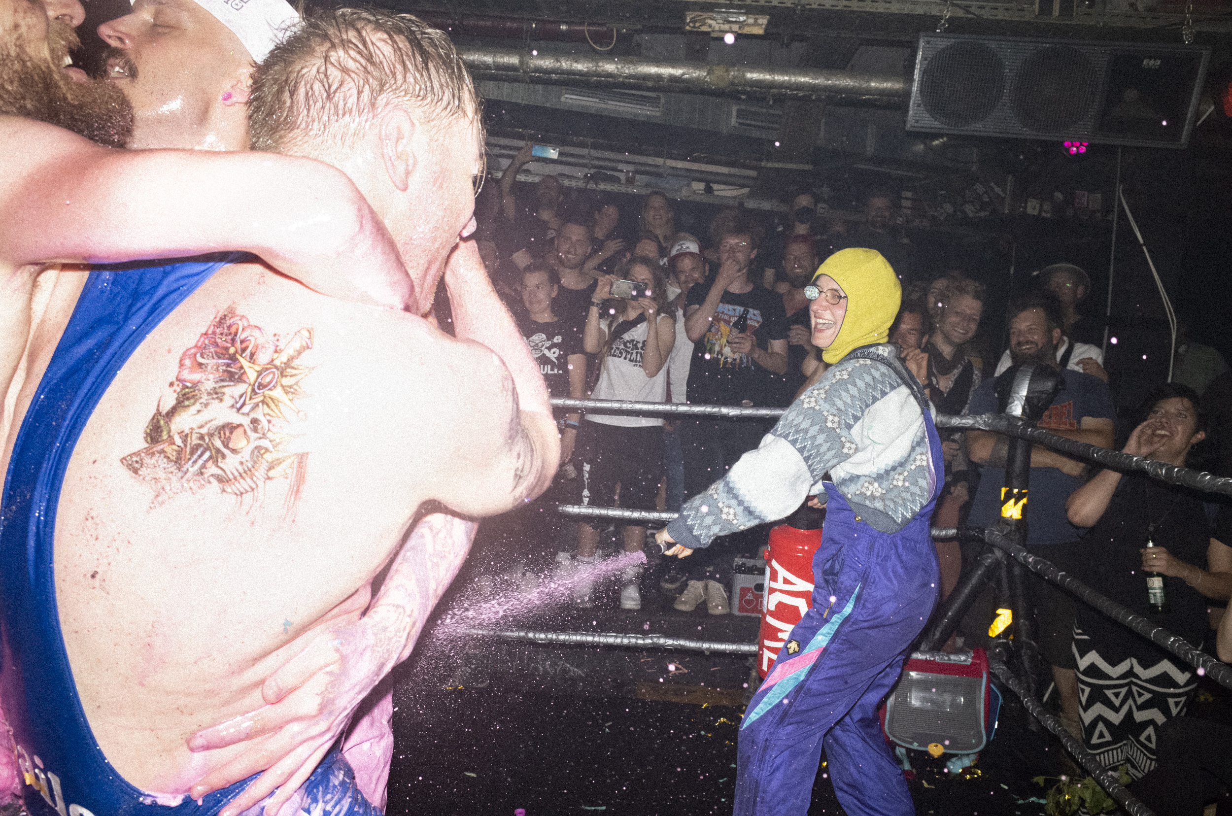 Eine Frau in einer Skihose sprüht rosa Pulver auf drei andere Wrestler.