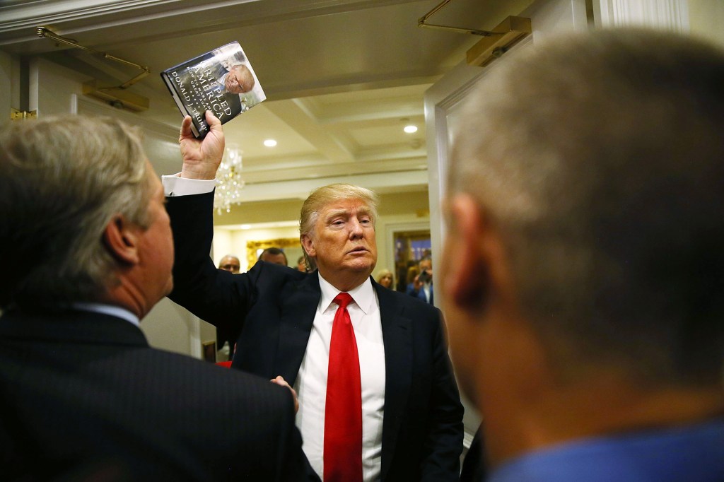 Trump holds up his book.