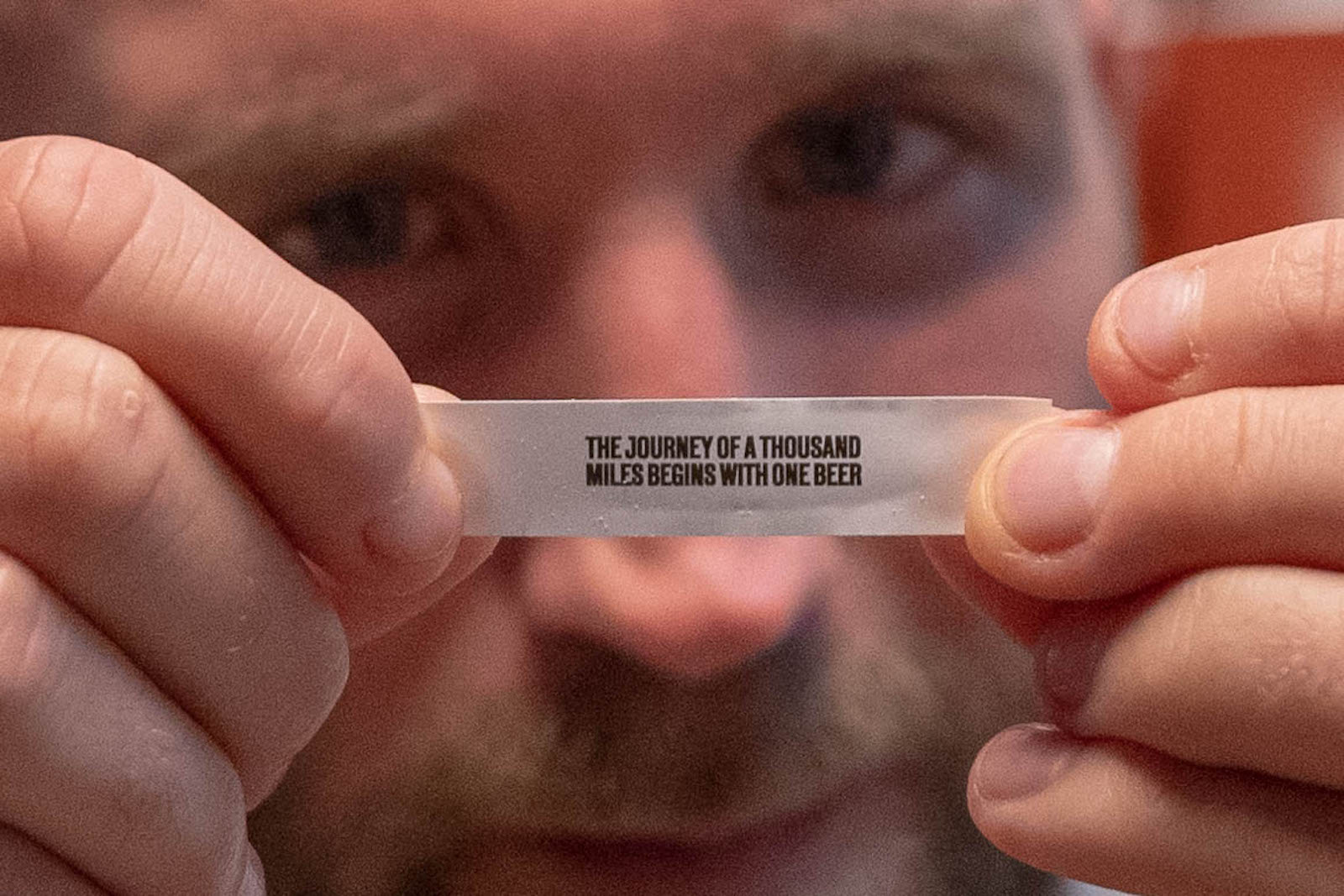 Writer Tom Usher holding a piece of paper with the phrase 'The journey of a thousand miles begins with one beer' printed on it