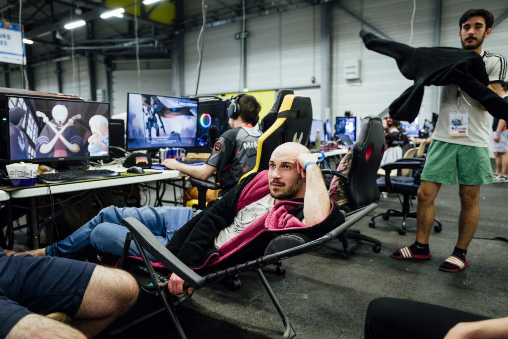 Gamers Assembly, LAN party – bald man reclining in a camping chair and talking to someone off camera.