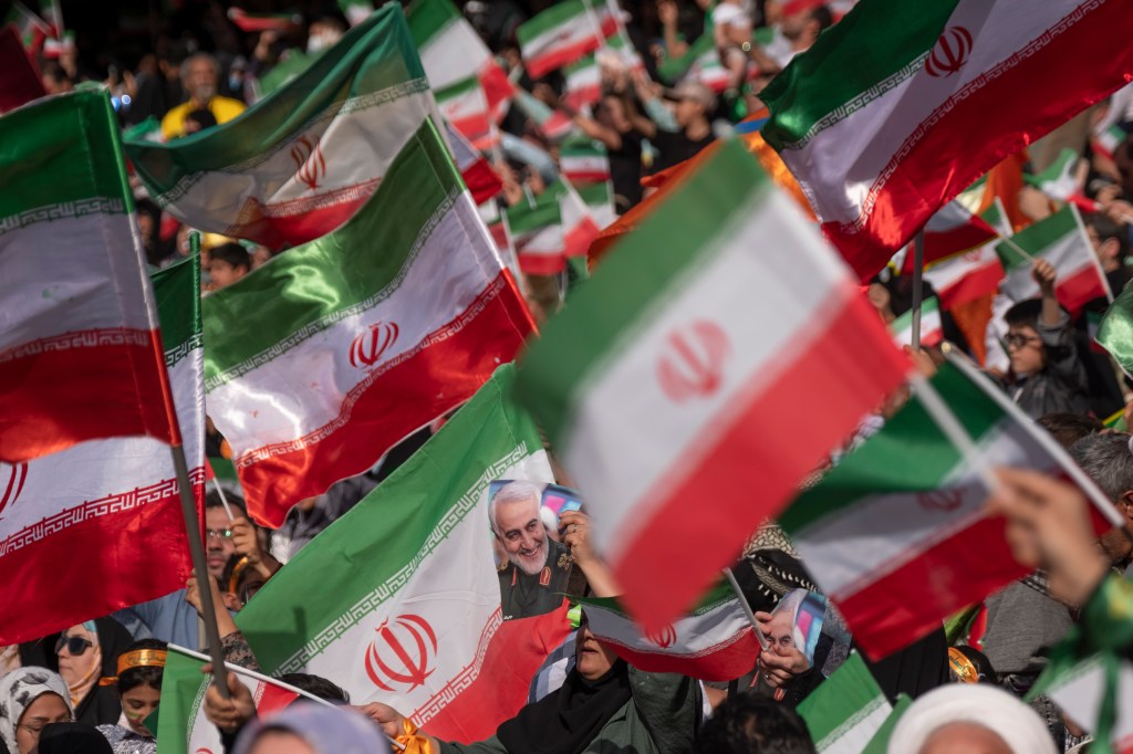 upporters of Irans Supreme Leader Ayatollah Ali Khamenei wave Iranian flags as one of them holds a portrait of former commander of IRGC Quds Force, General Qasem Soleimani, during a gathering to chant the Hymn Hello Commander at the one hundred thousand s