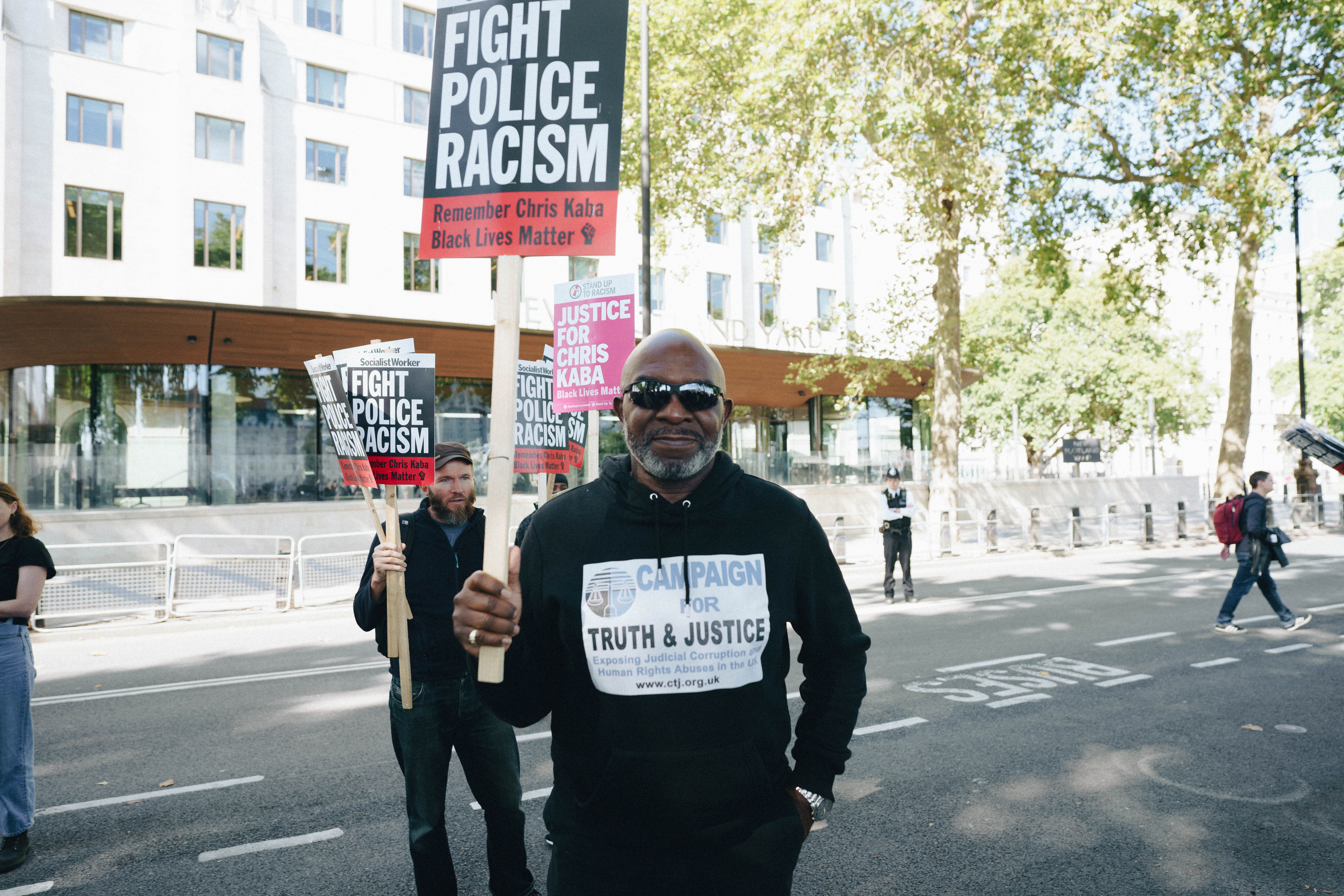 Man in sunglasses holding a Fight Police Racism sign at Chris Kaba protest