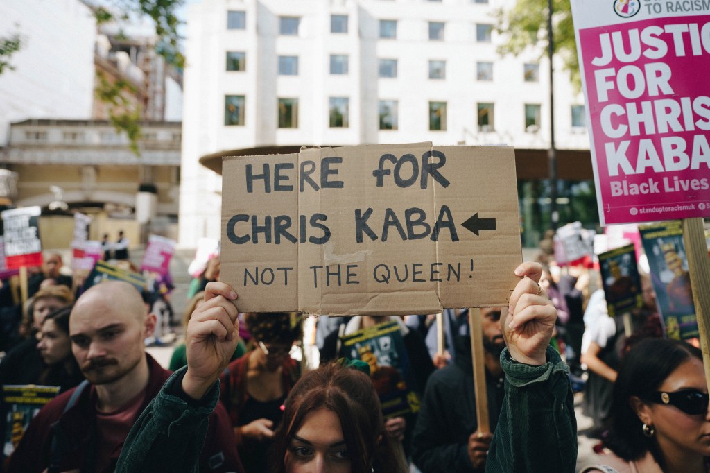 Person at the Chris Kaba protest with a sign reading "Here for Chris Kaba, Not the Queen"