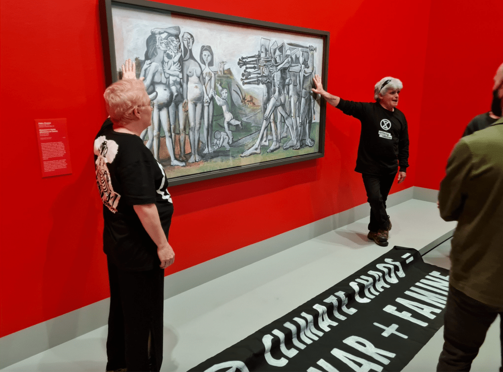 Two climate activists with their hands glued to painting