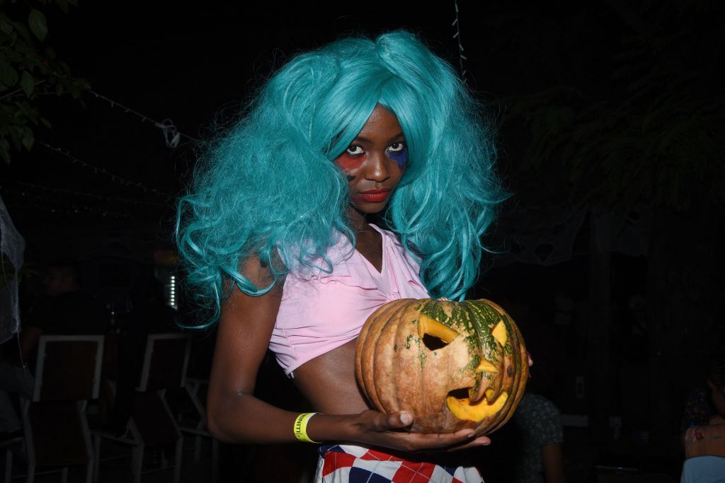 A woman in a blue wig holding a jack-o'-lantern.