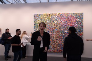 A smiling man next to a Damien Hirst at Frieze Art Fair