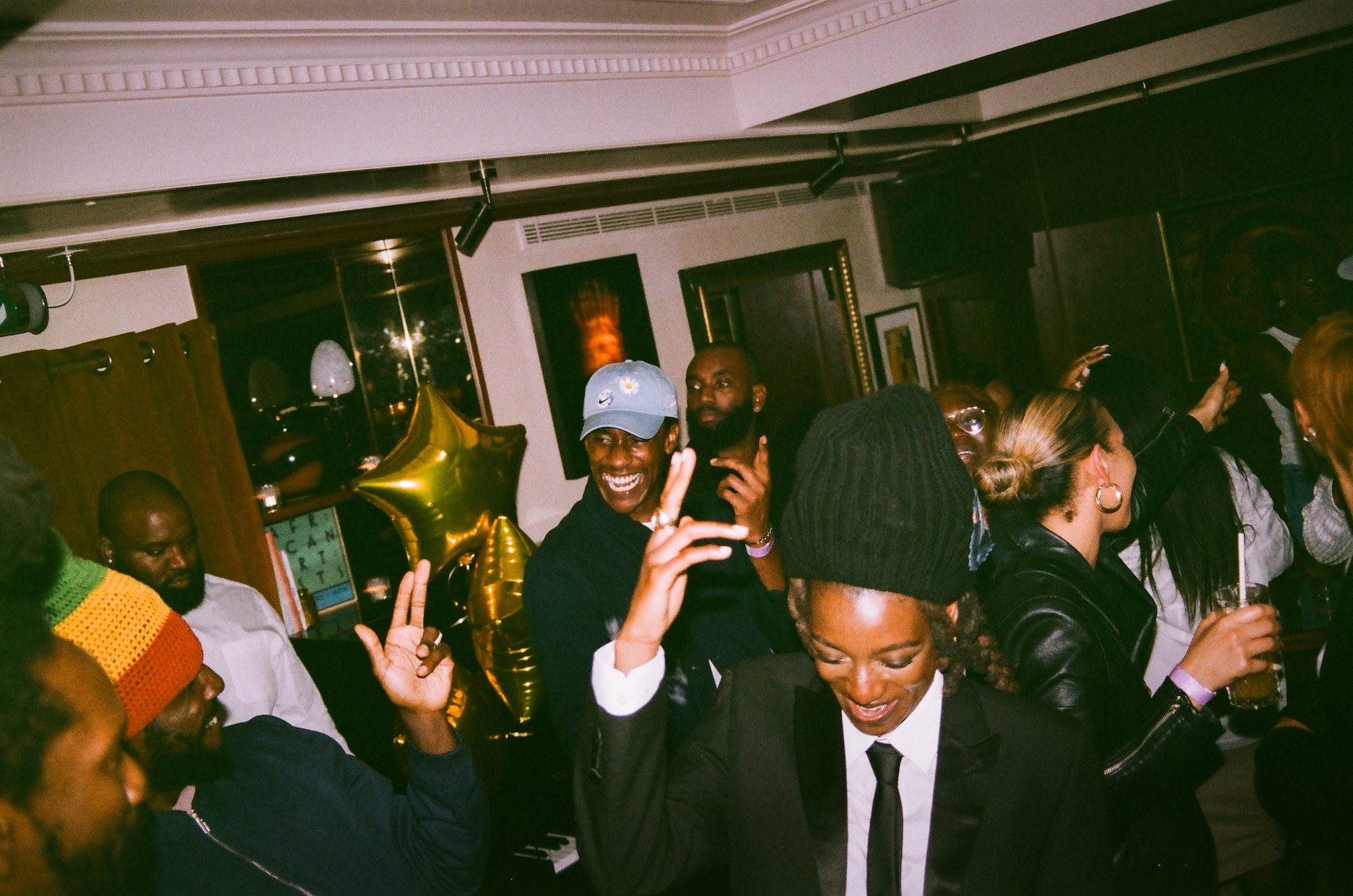 Little Simz dans un bonnet noir levant des doigts de pistolet lors d'une fête, photographié par Eddie Otchere