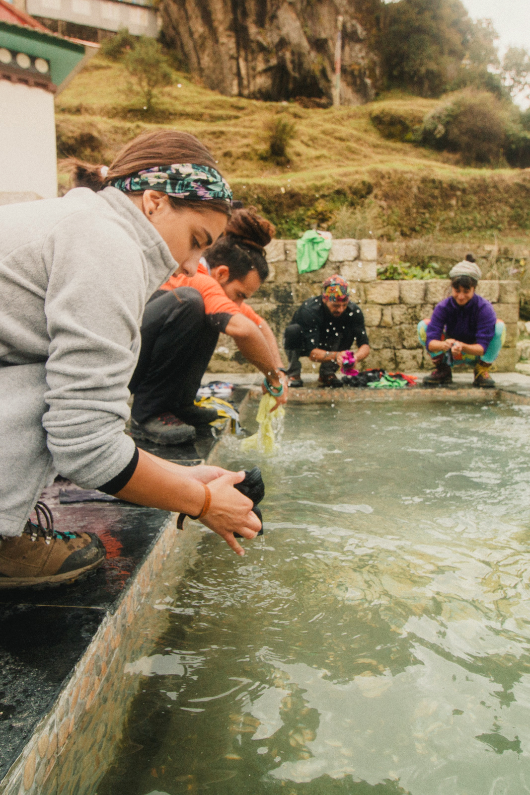 Namche bazar – group of four people (two men and two women) wearing activewear, squatting near a shallow basin to wash their clothes