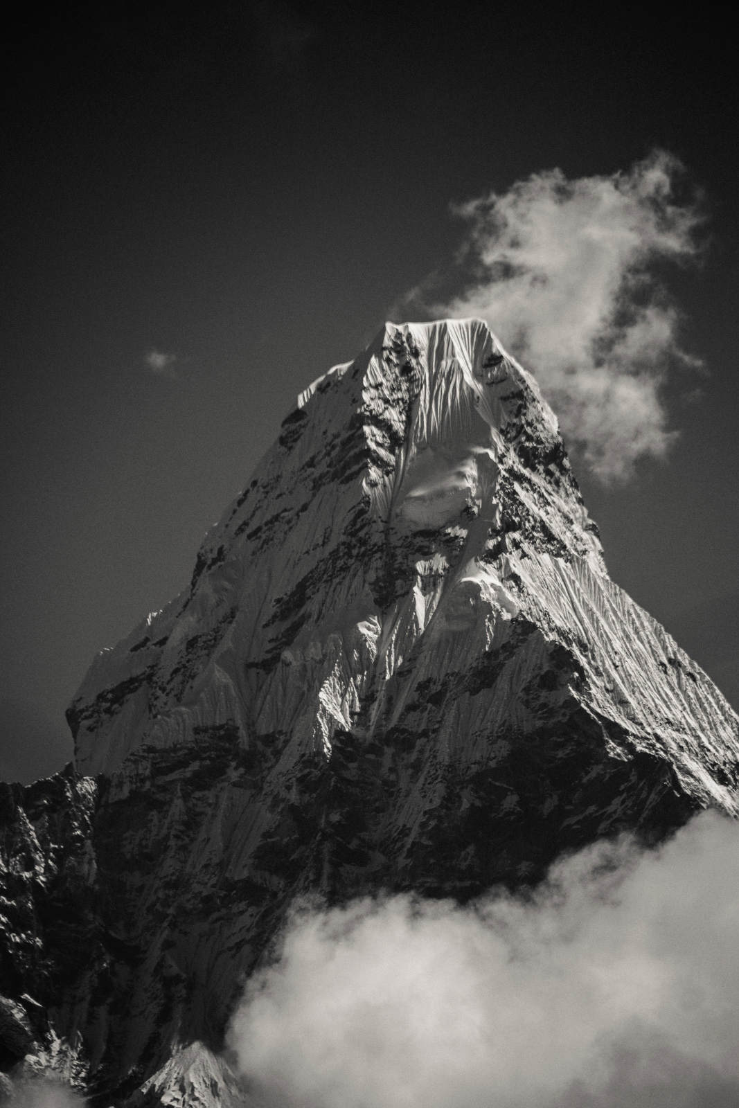 Ama Dablam, Nepal – Schwarz-Weiß-Foto eines scharfkantigen, schneebedeckten und von dünnen Wolken umgebenen Berggipfels.