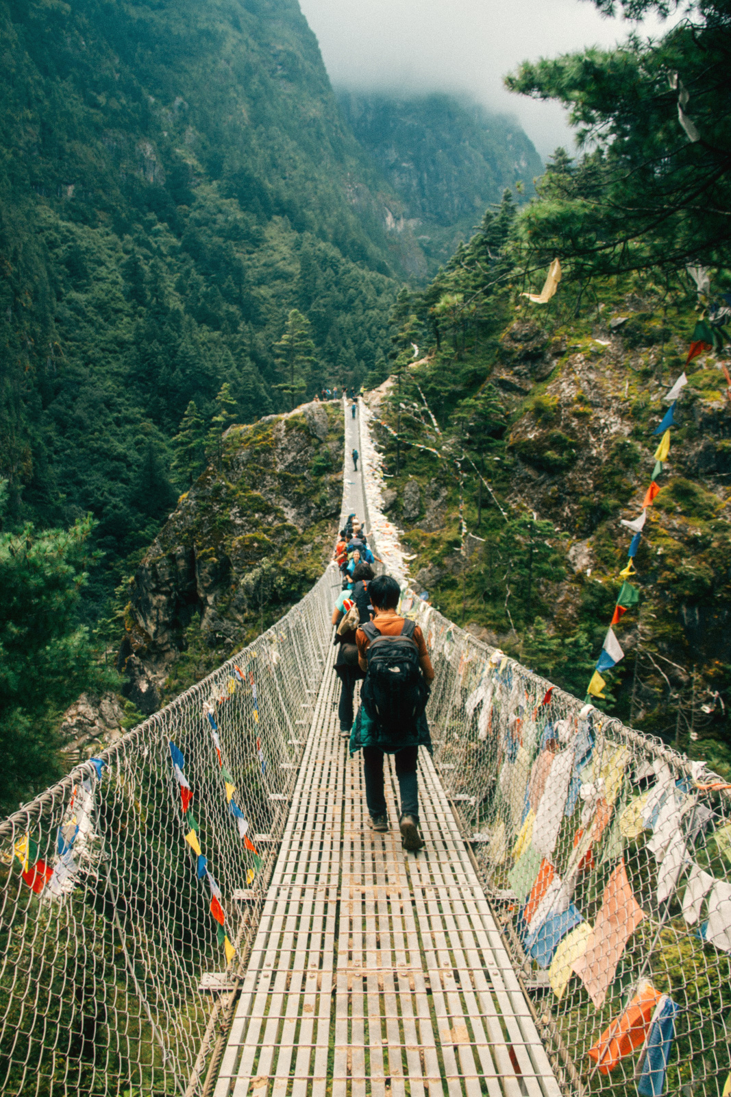 Hillary Bridge, Nepal – long narrow suspended bridge with nets on either side and a long single file of trekkers.