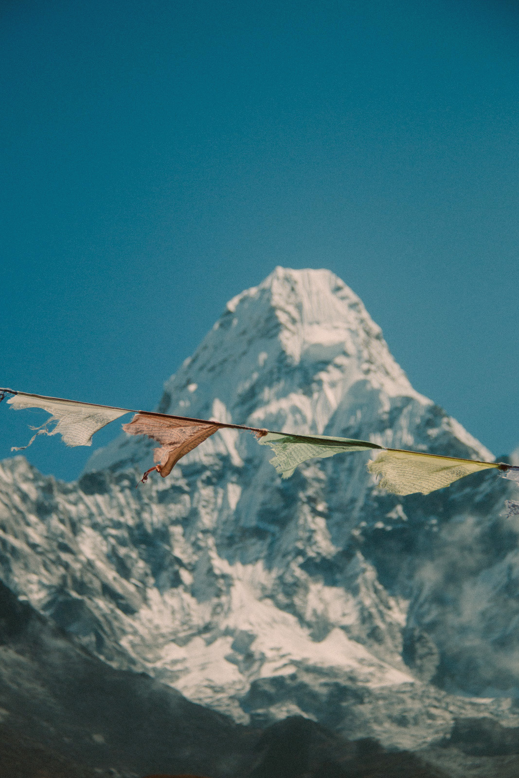 Von Tengboche nach Dyngboche, Ama Dablam, Nepal – Foto eines verschneiten Berggipfels, davor eine Reihe tibetischer Gebetsfahnen.