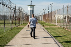 A prisoner walks thru a fenced section toward a guard tower at Angola Prison .