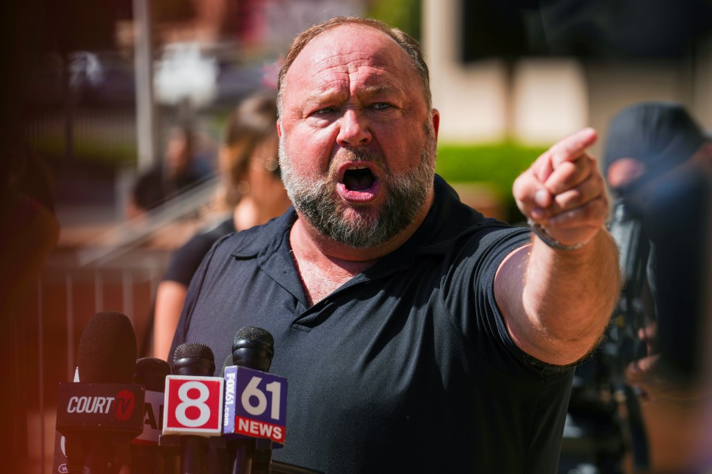 Alex Jones is red-faced, pointing and open-mouthed in front a bank of microphones.