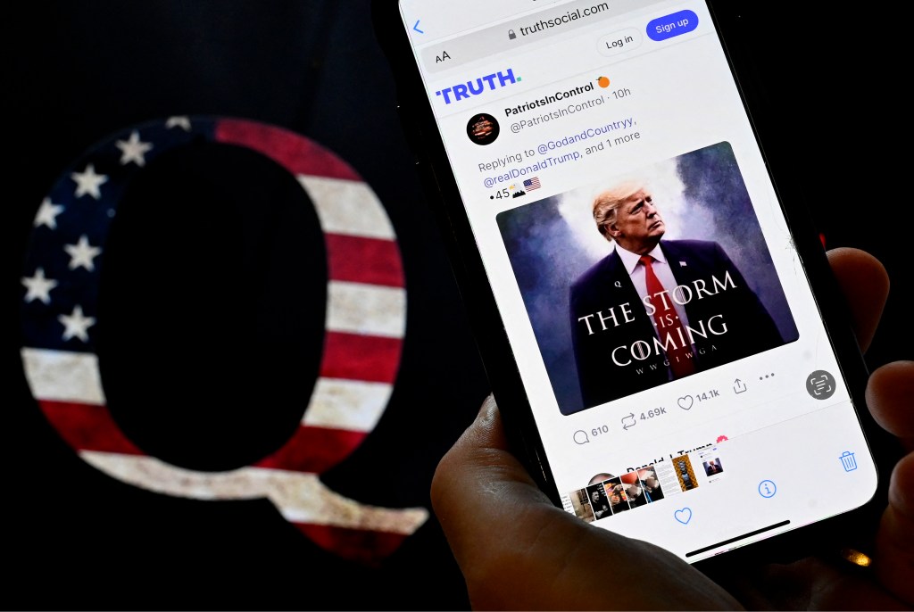 In this photo illustration, Donald Trump's TRUTH Social account is seen on a mobile device with an image of a QAnon sticker in the background in Washington, DC on September 13, 2022.