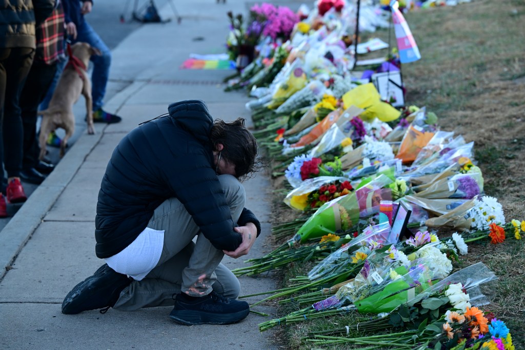 A mourner places kneels at a makeshift memorial near Club Q on November 20, 2022 in Colorado Springs, Colorado.​