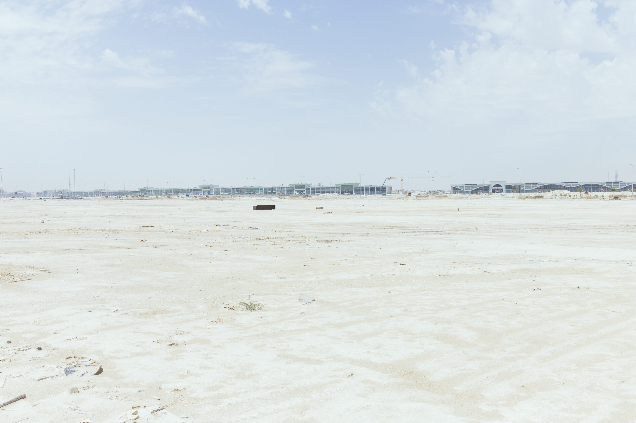 Eine flache Wüstenlandschaft mit langen Gebäuden am Horizont