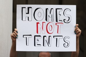 Protester holds "homes not tents" sign