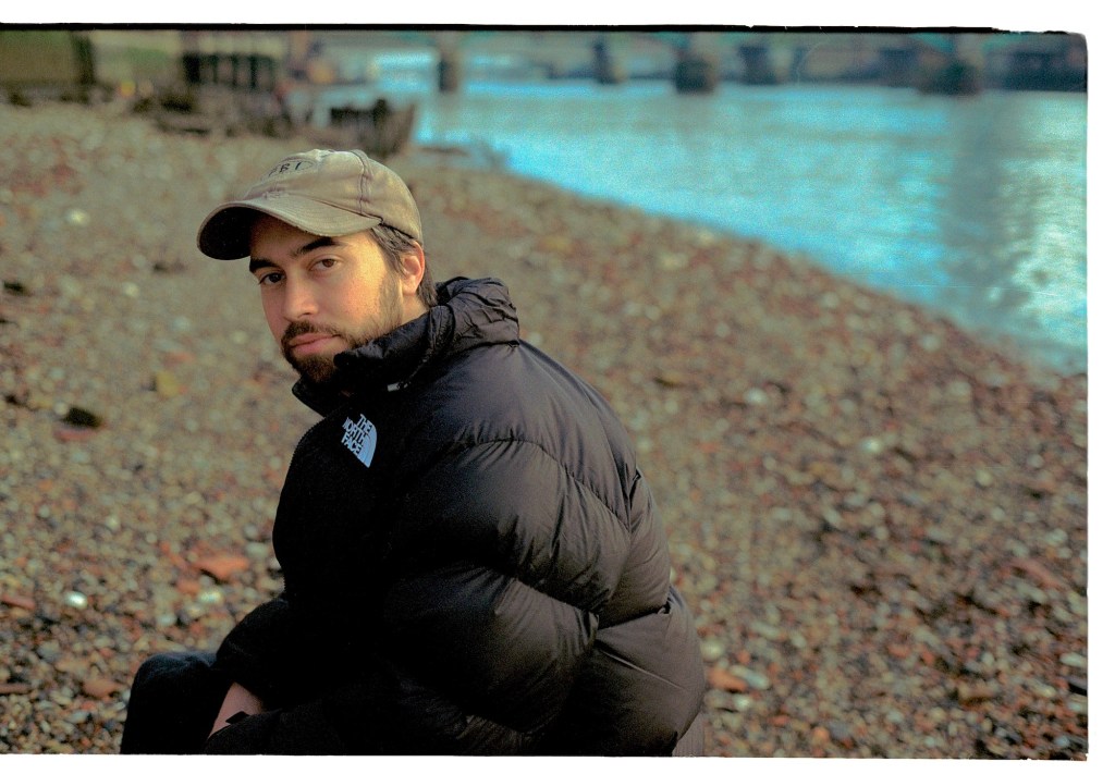 Alex G sitting by the Thames in a North Face Jacket