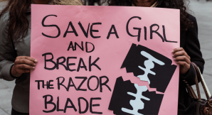 Poster merah muda bertuliskan “Save a Girl and Break the Razor Blade” dalam pawai menentang praktik sunat perempuan. Foto: Bmarcos del Mazo/Lightrocket via Getty Images